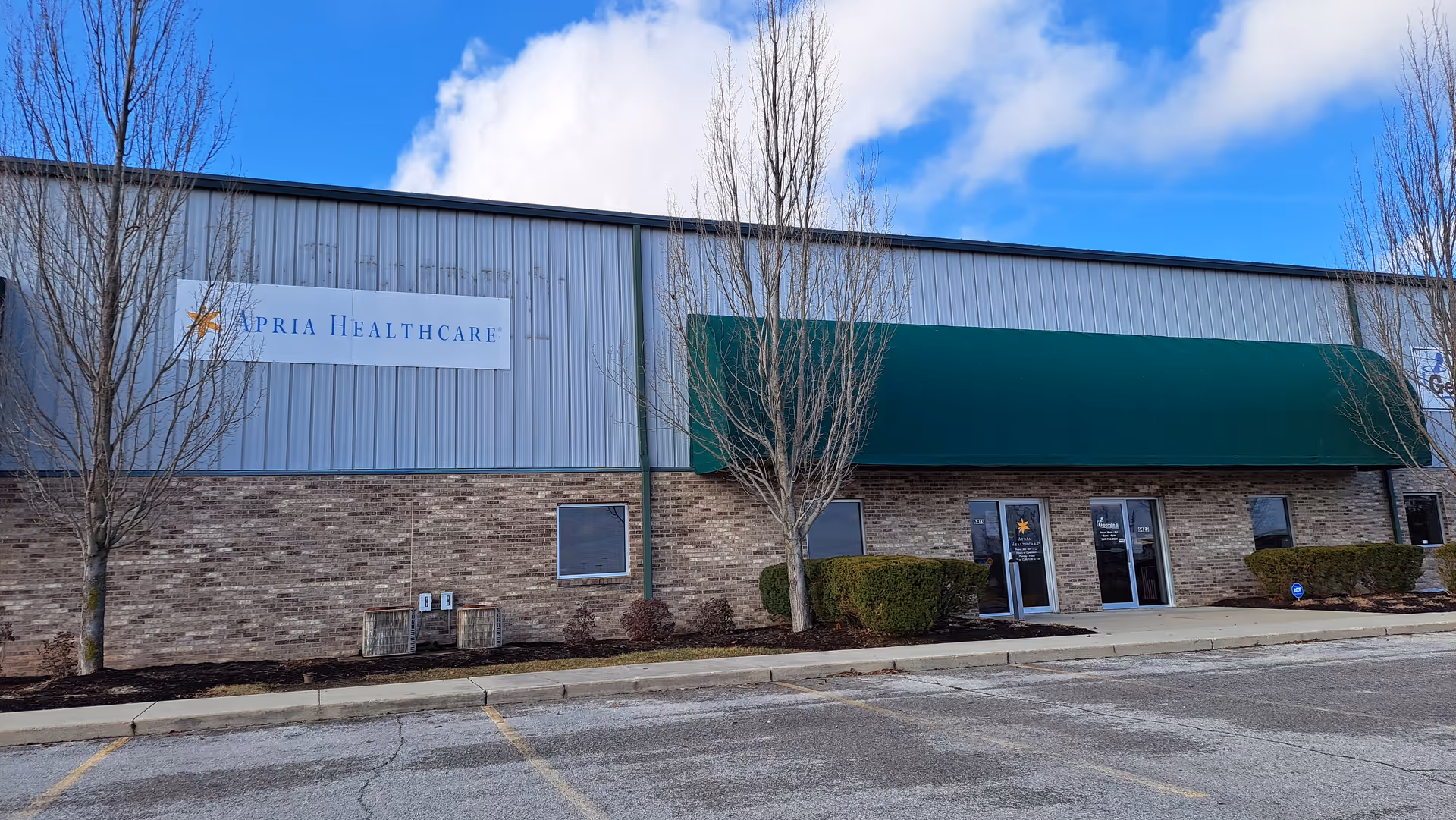 Exterior view of Apria Healthcare building with a green awning and trees.