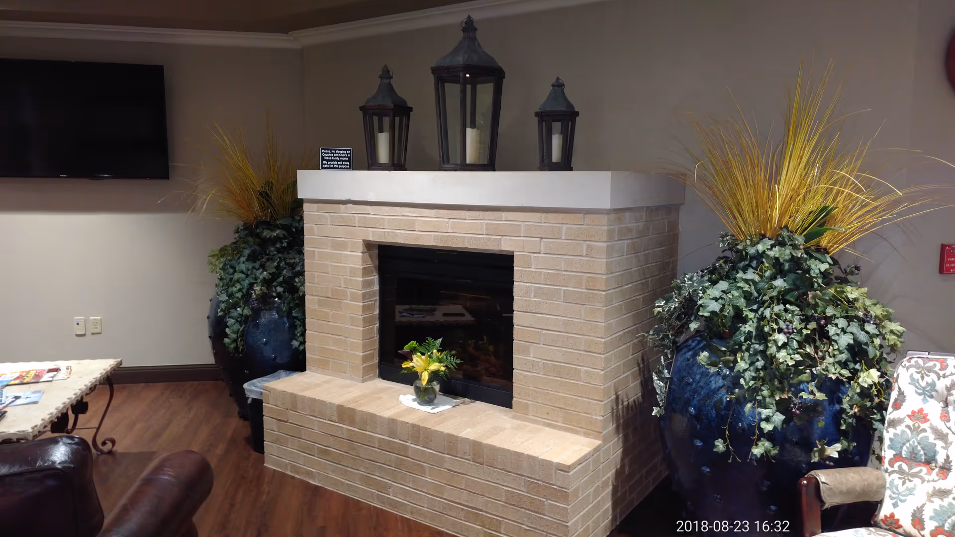 Indoor lounge with a brick fireplace, large planters, and a wall-mounted TV.