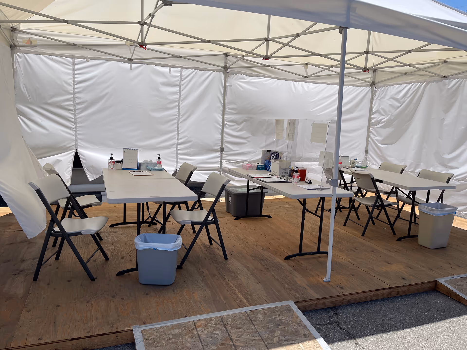 Outdoor white canopy with folding tables, chairs, and supplies for a temporary intake setup.
