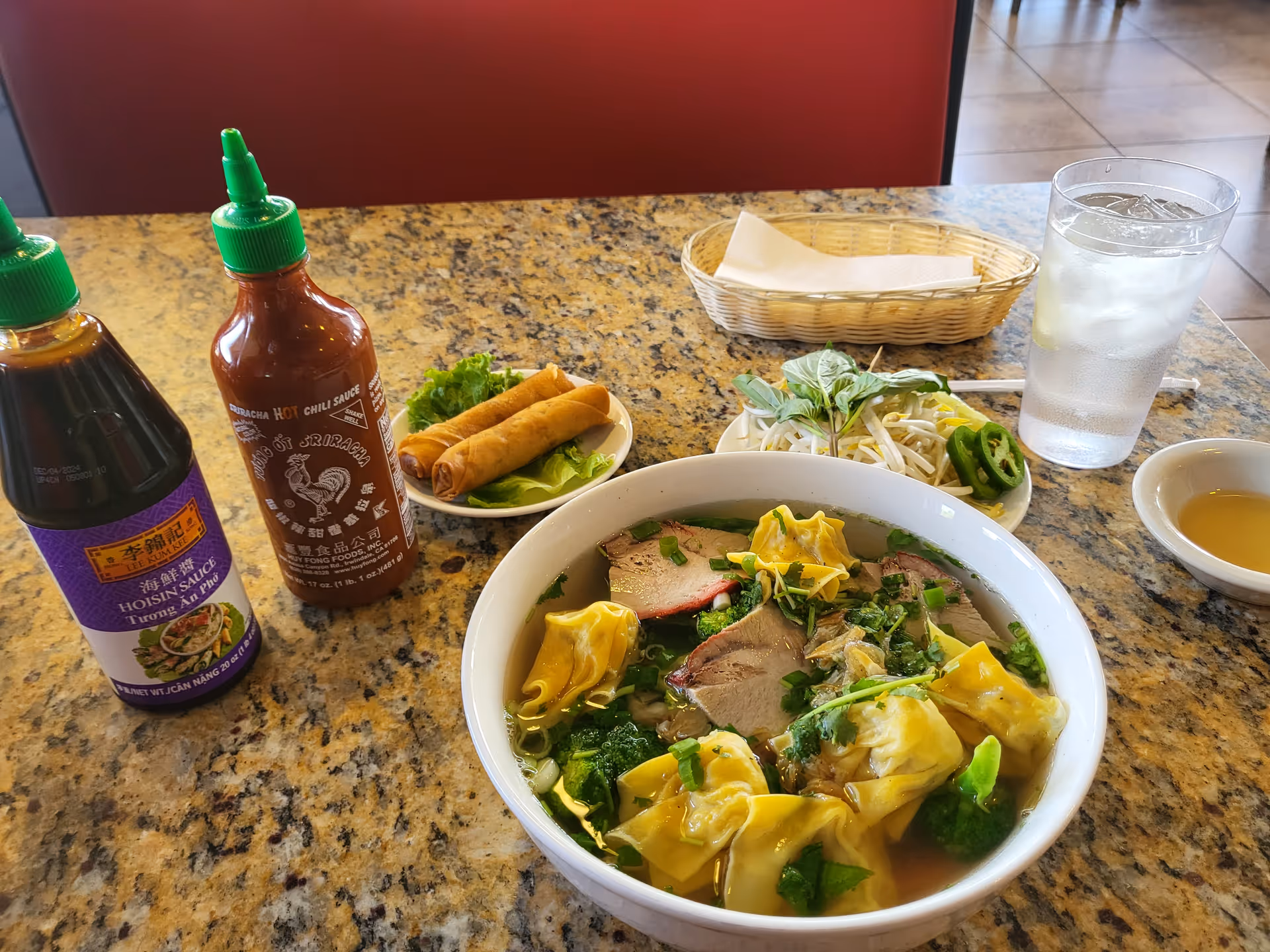 Table with dumplings, wonton soup, sauces, and a glass of water in dining setting.