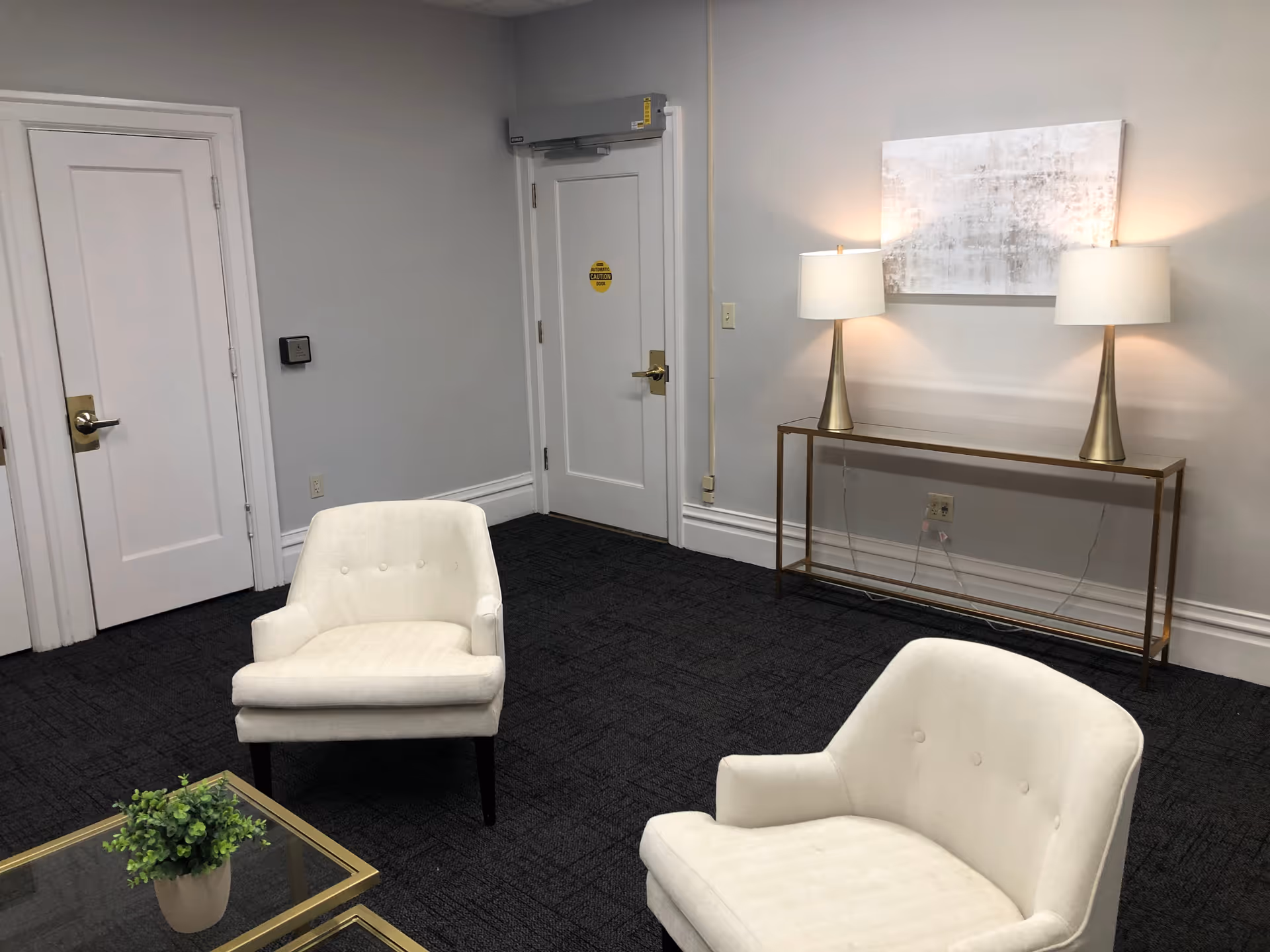 A quiet senior living facility lounge with two white chairs, a glass coffee table, and lamps.