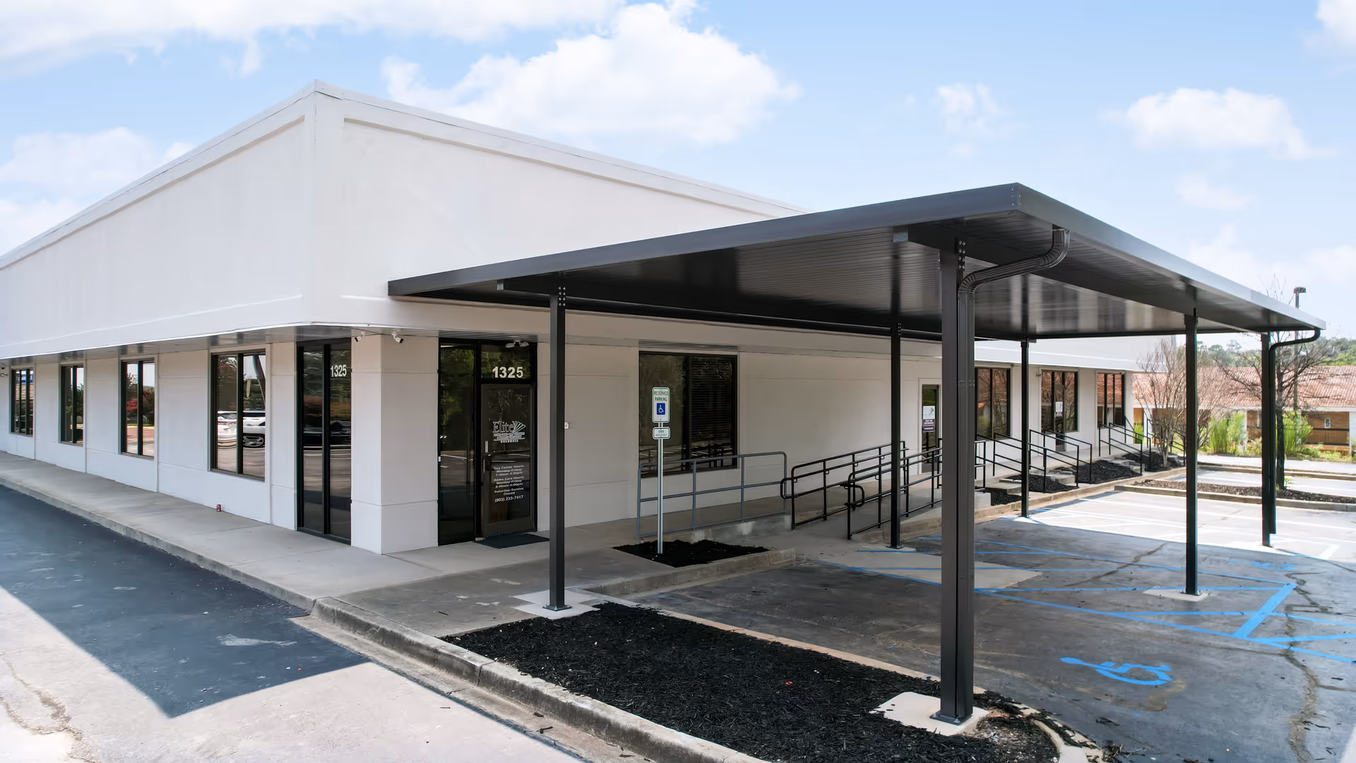 Exterior view of a single-story white building with a covered entrance and parking area.