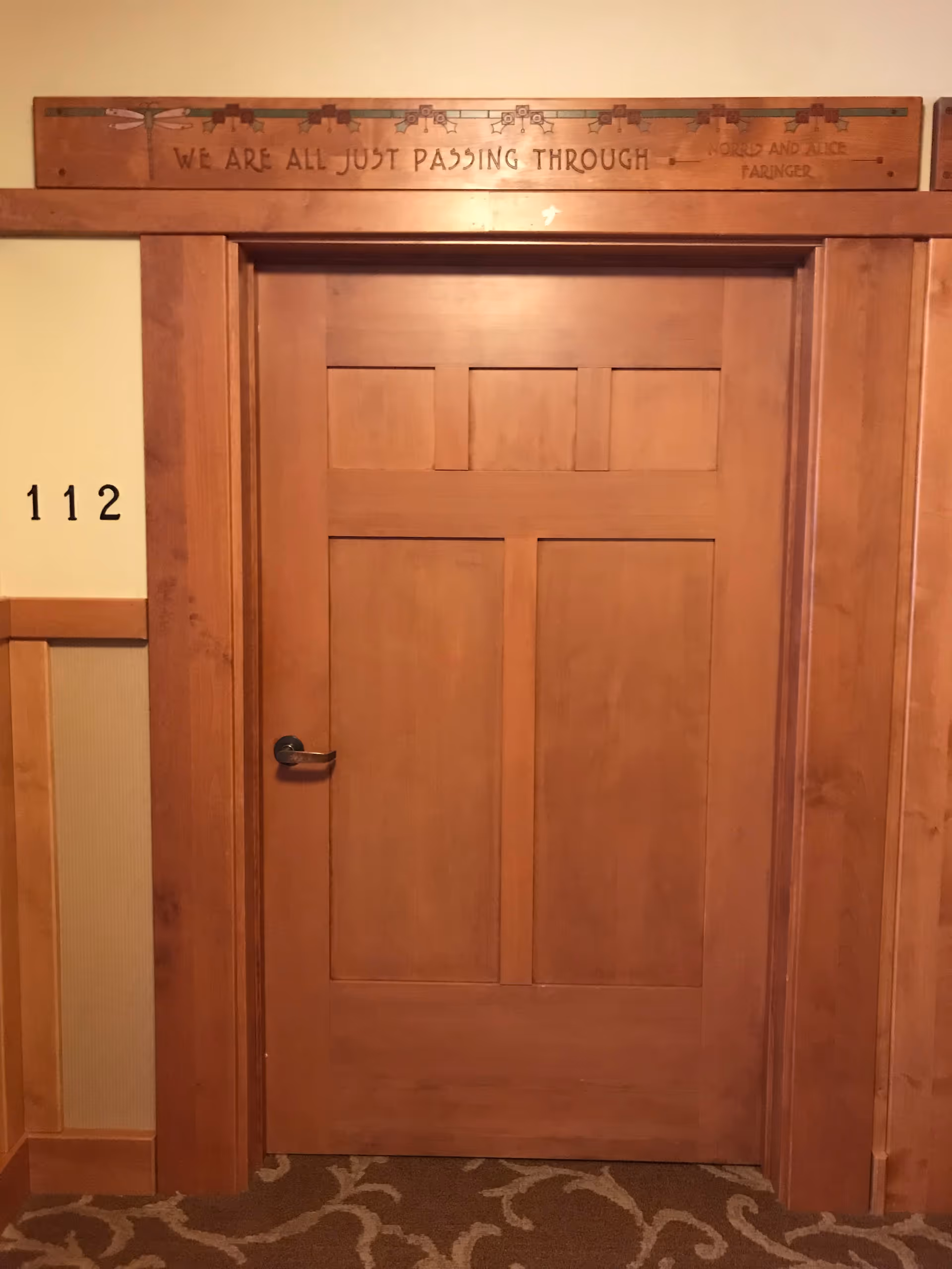Wooden door in a wood-paneled hallway with a carved sign above and room 112.