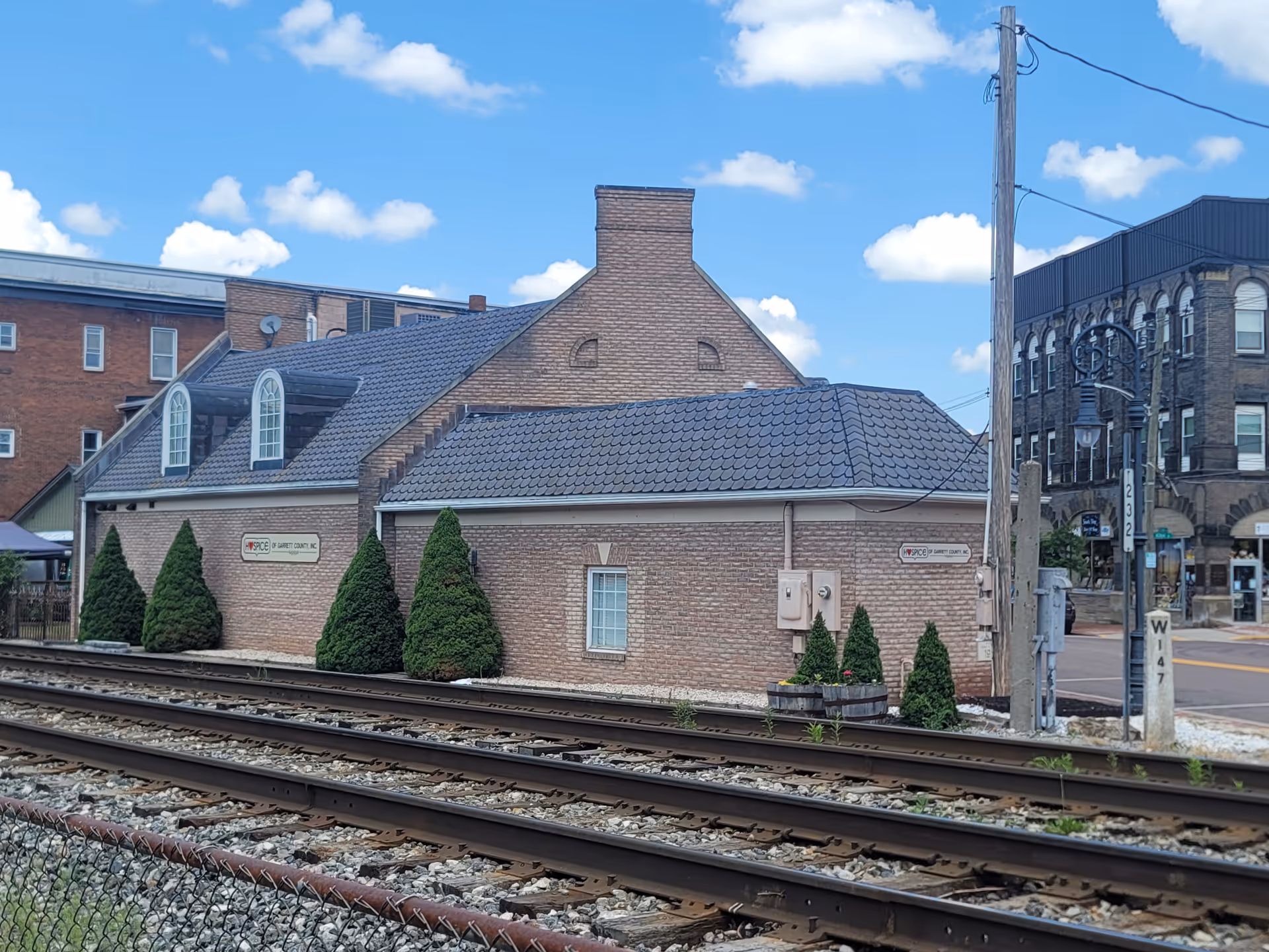 Brick Hospice of Garrett County building along railroad tracks under a blue sky.