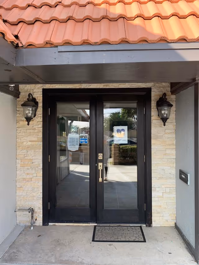 Exterior double glass doors framed by stone walls, lantern lights, and a mat at the entrance.