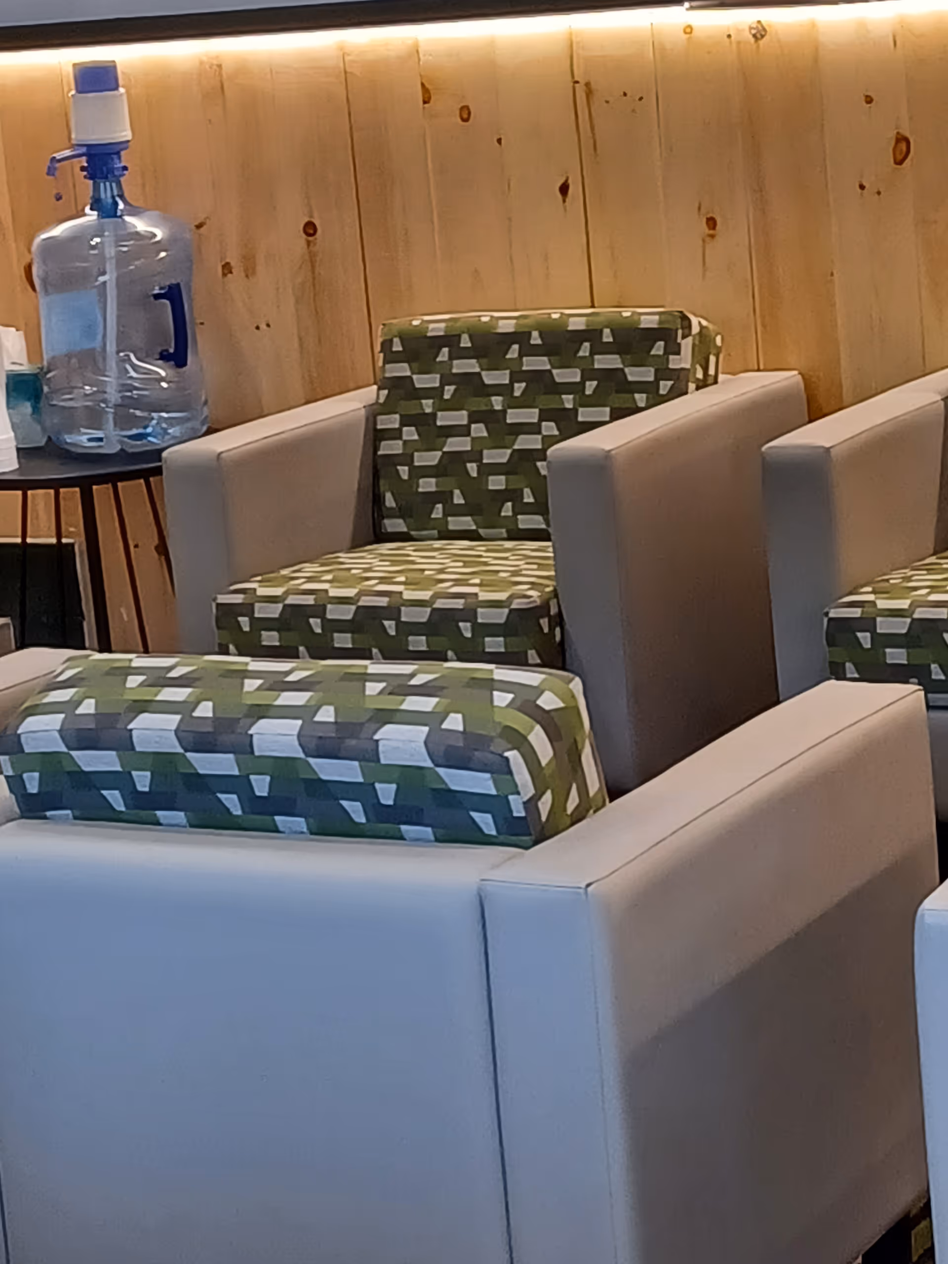 Interior lounge with white chairs, green patterned cushions, wood-paneled wall, and a water dispenser.
