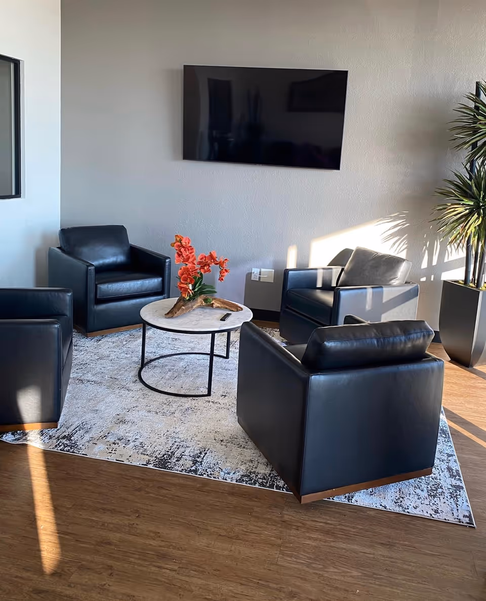 Modern lounge area with black leather chairs, a round marble table, and a wall-mounted TV.