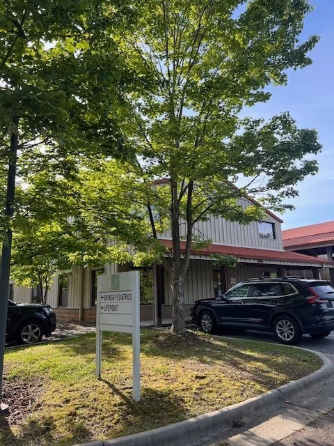 Exterior view of a BAYADA Pediatrics building with trees, sign, and parked cars.