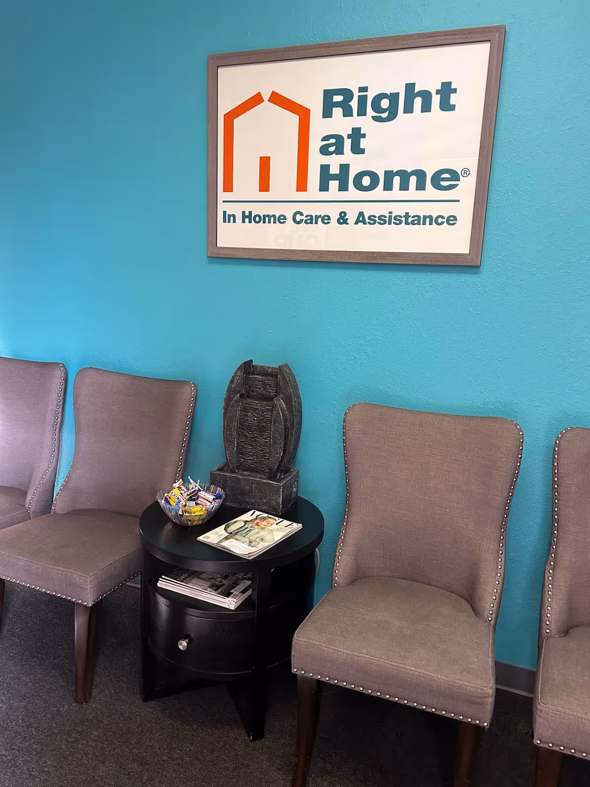 Teal-walled waiting area with Right at Home sign, beige chairs, a black side table, and magazines.