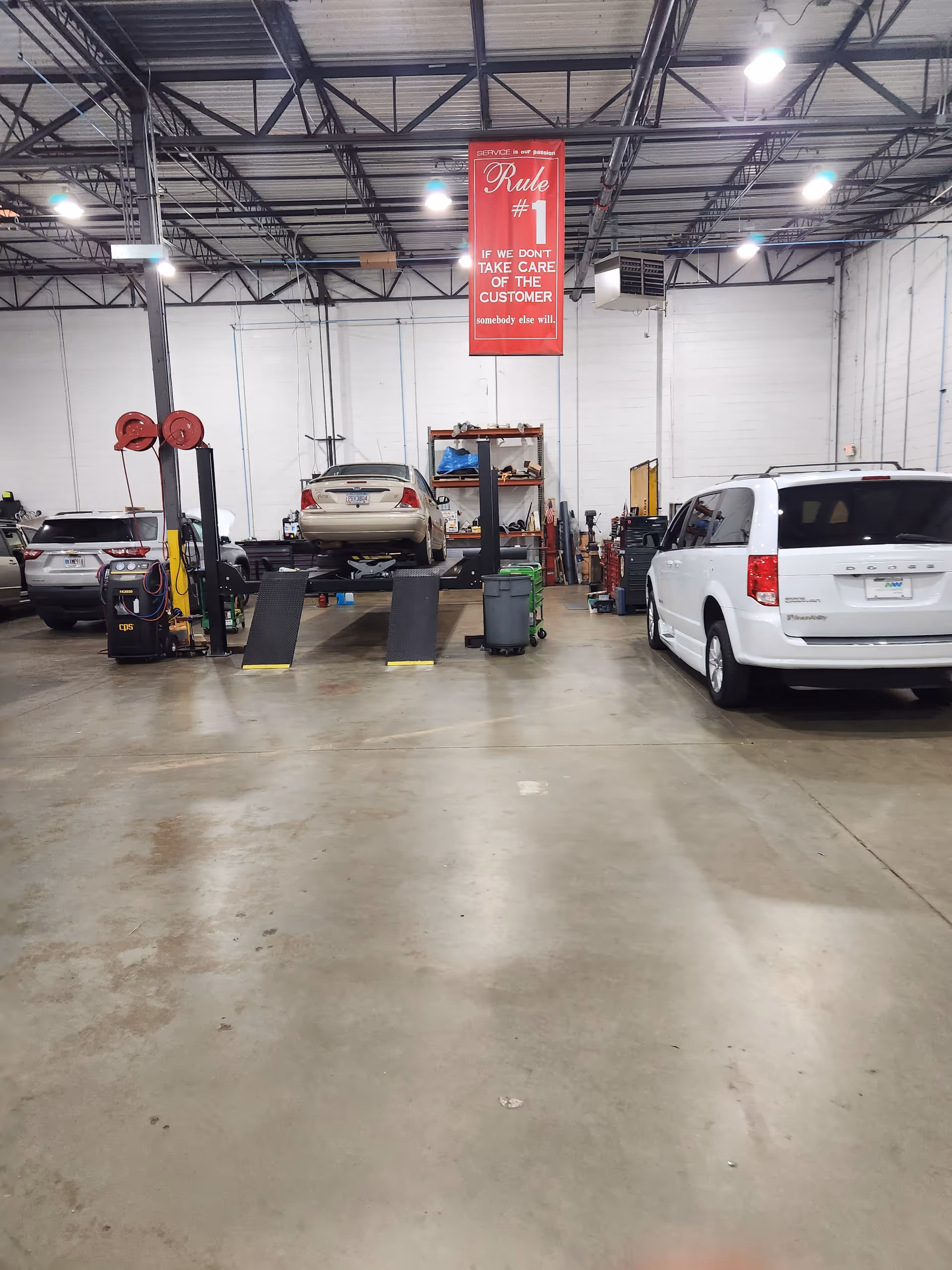 Interior of a large automotive workshop with a lifted car and equipment.