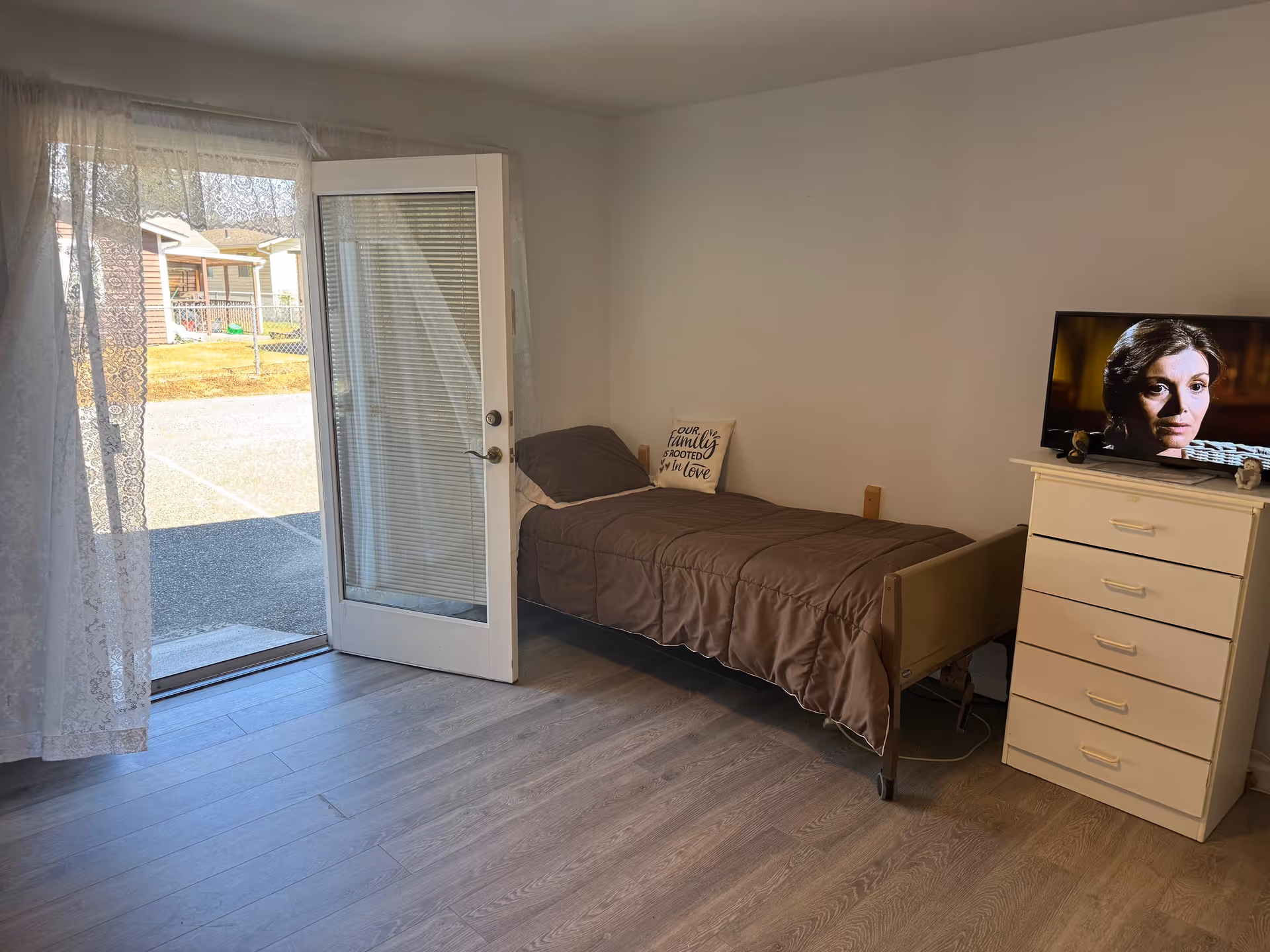 Small bedroom with single bed, dresser, TV, and glass door opening to outside.