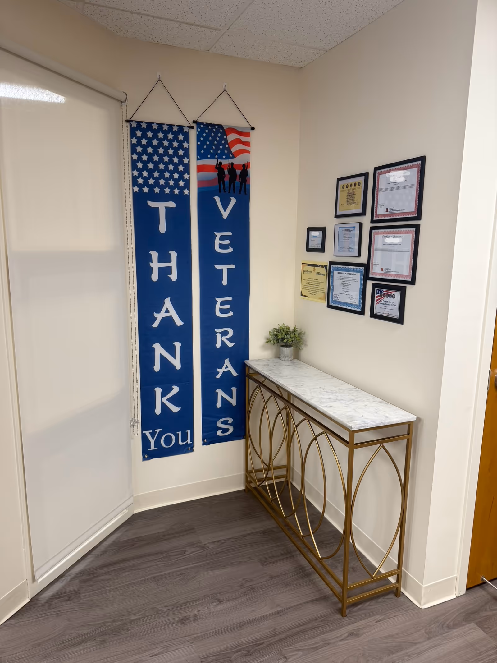 Narrow hallway corner with patriotic 'Thank You Veterans' banners, a marble-topped console table, and framed awards.