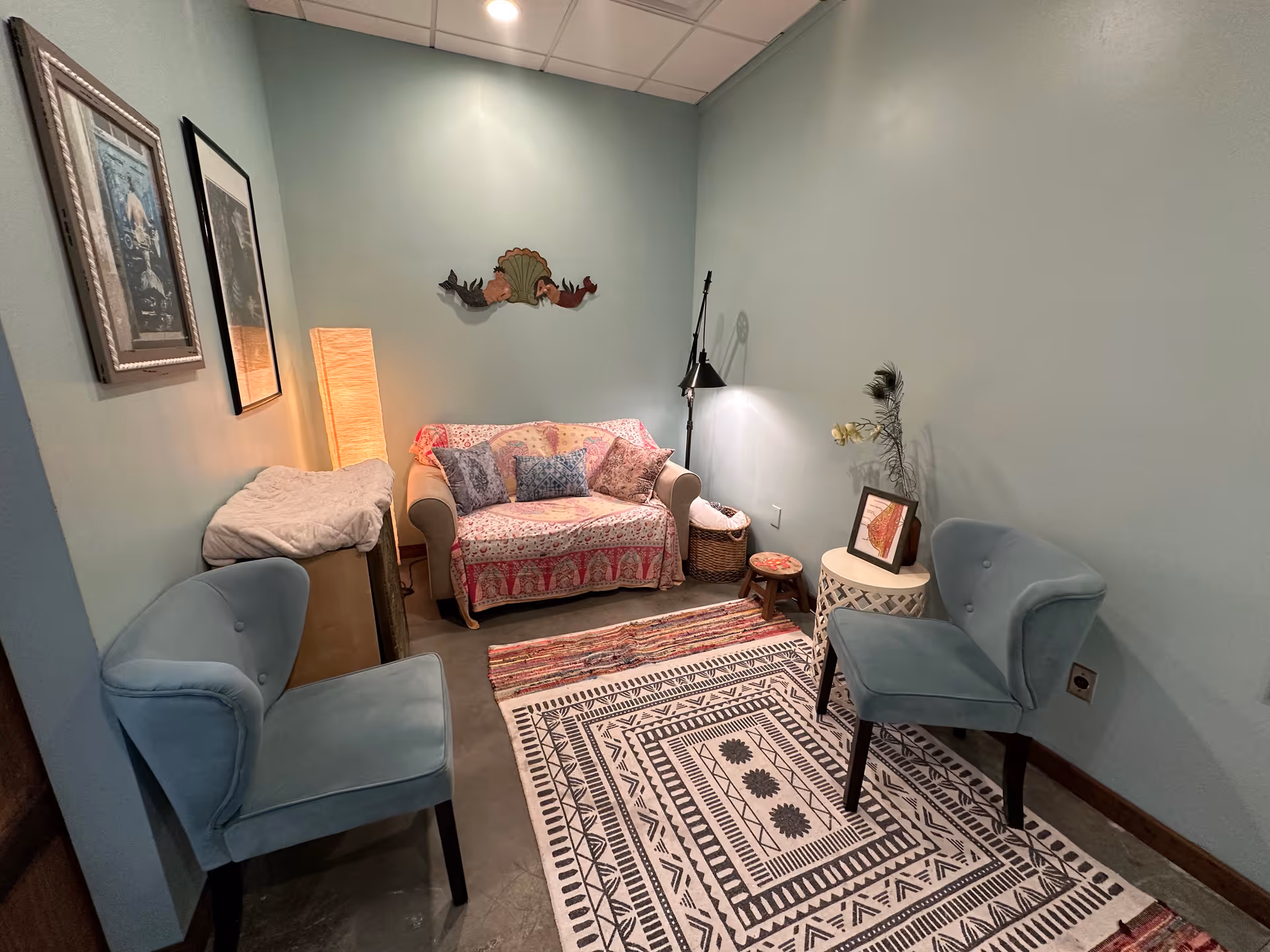 Cozy teal-walled lounge with a pink-printed sofa, two blue chairs, and a patterned rug.