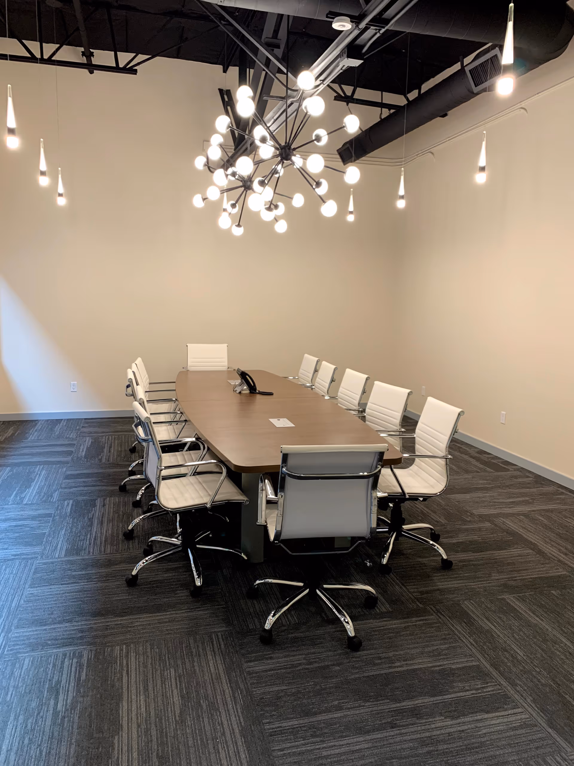 Modern conference room with a long wooden table, white chairs, and an intricate chandelier.