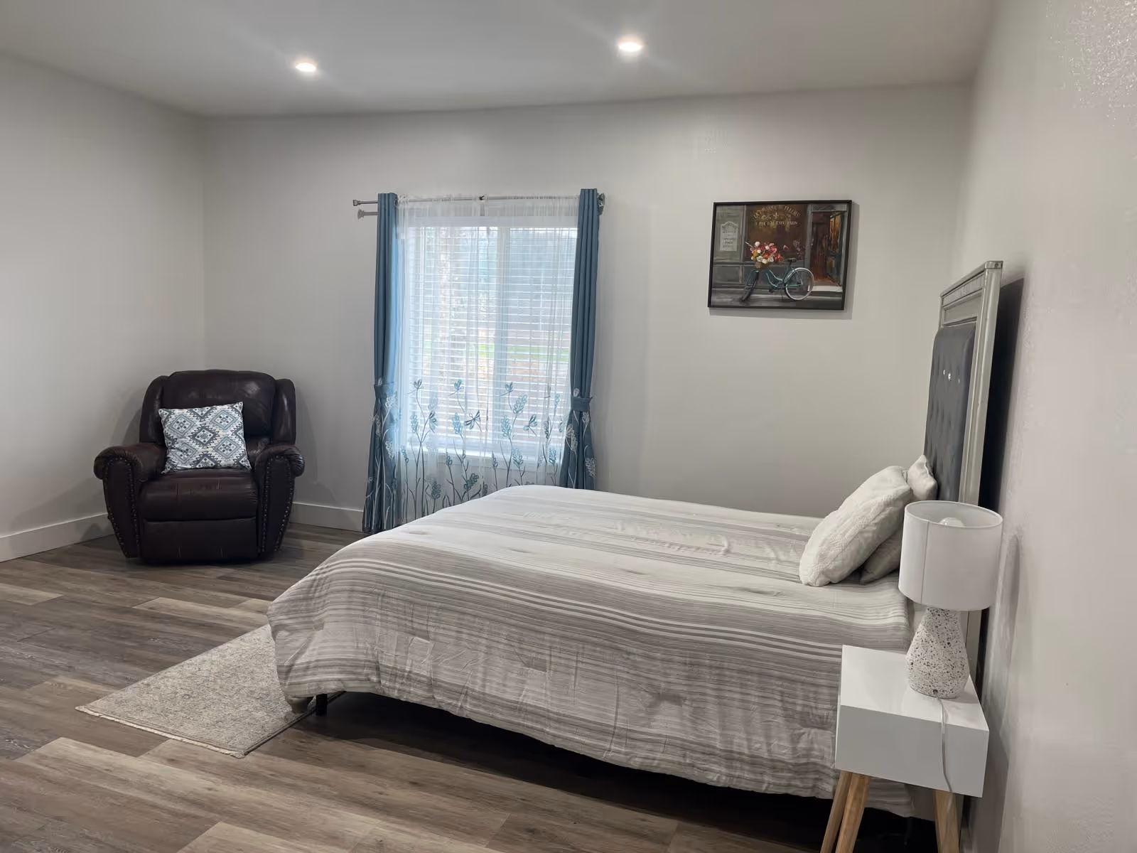 Furnished bedroom with a bed, nightstand, lamp, chair, and window.
