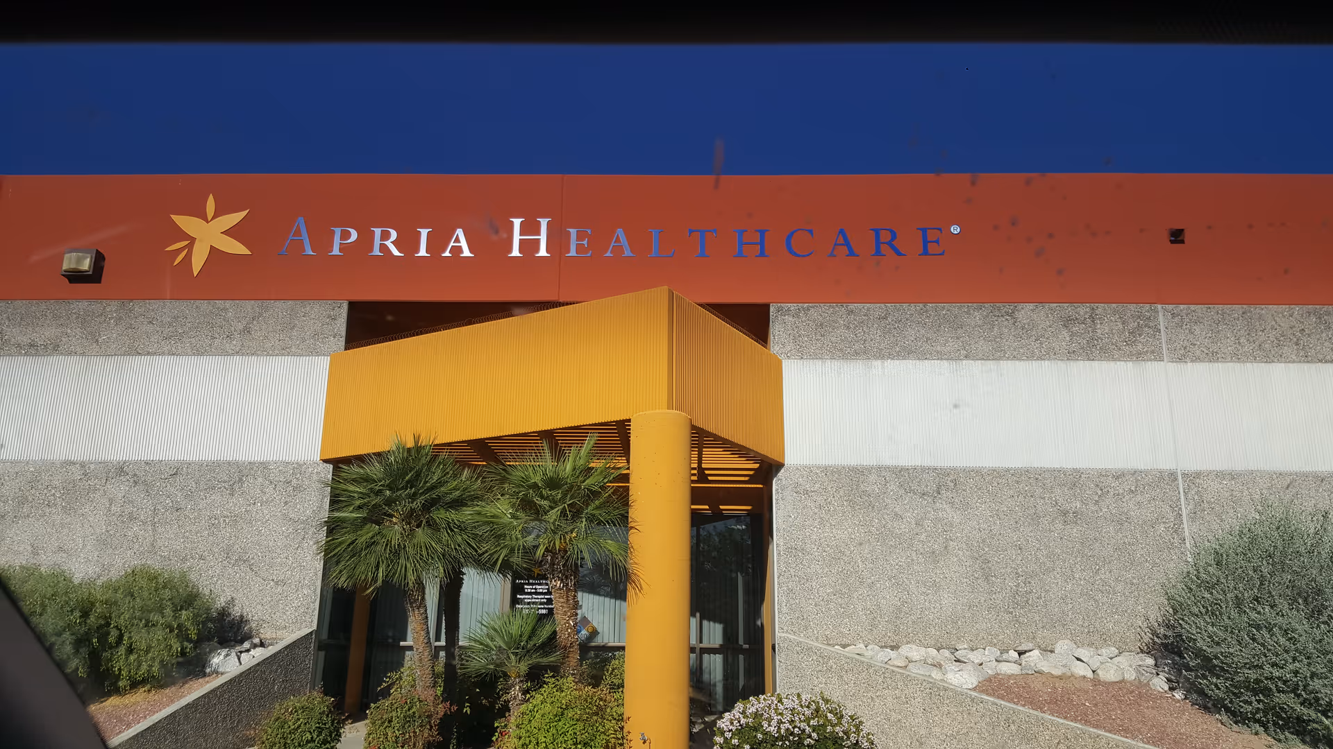 Exterior view of Apria Healthcare building with orange entrance canopy and palm trees