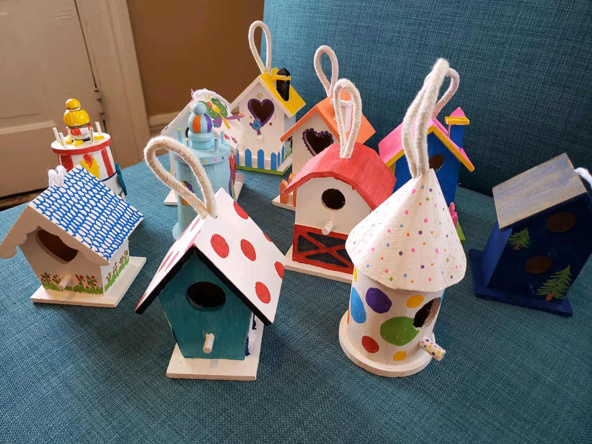 Colorful handmade birdhouse crafts arranged on a teal table in an interior room.