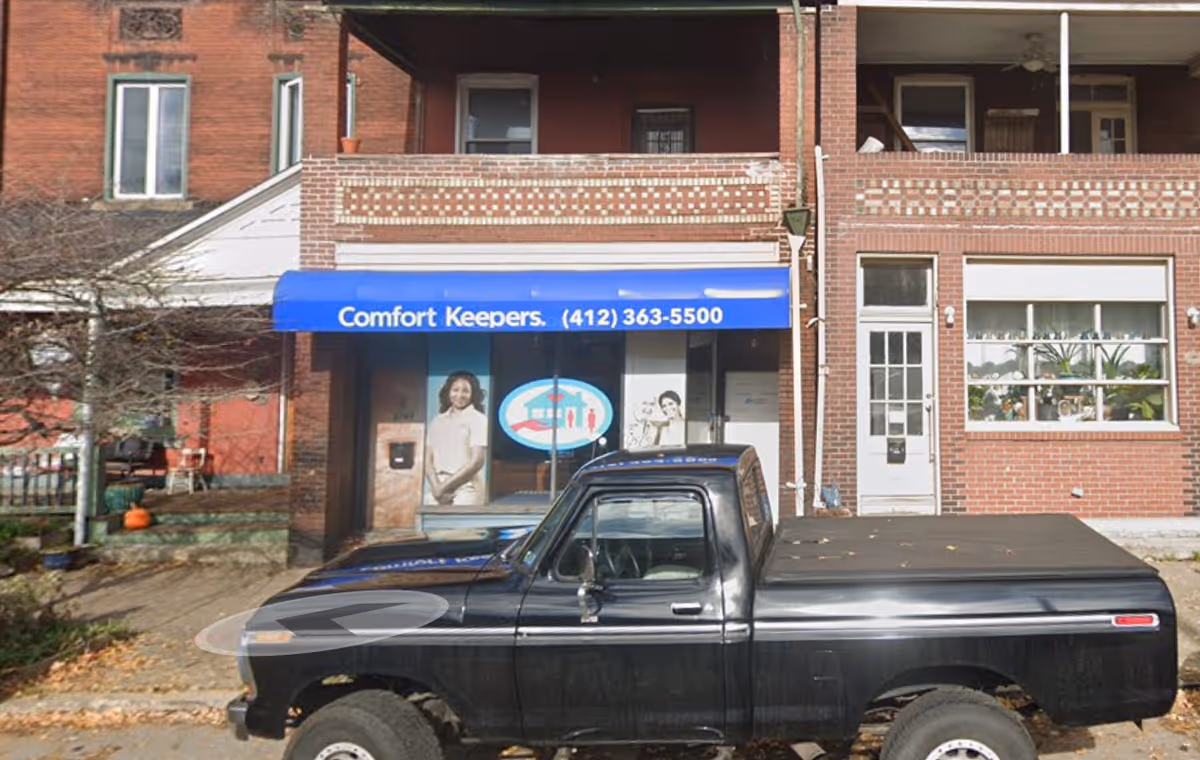 Exterior view of Comfort Keepers storefront with blue awning and a black pickup truck.