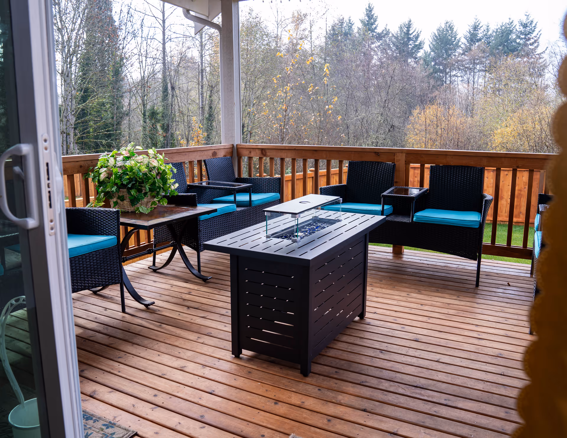 Outdoor wooden deck with black wicker seating, teal cushions, and a central fire pit.