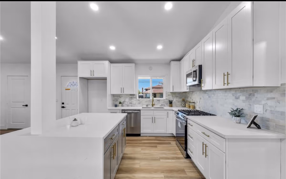 Bright white kitchen with island, stainless steel appliances, and tiled backsplash.