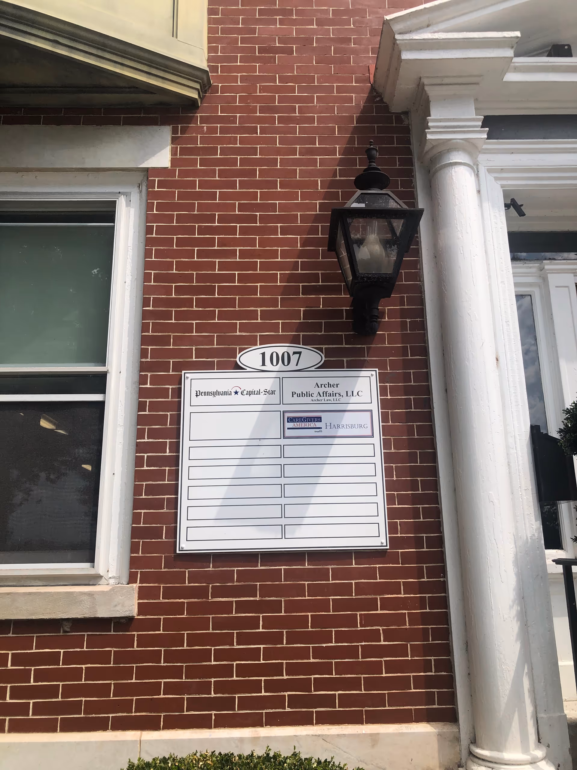 Brick building exterior with a wall-mounted directory sign and a lantern.