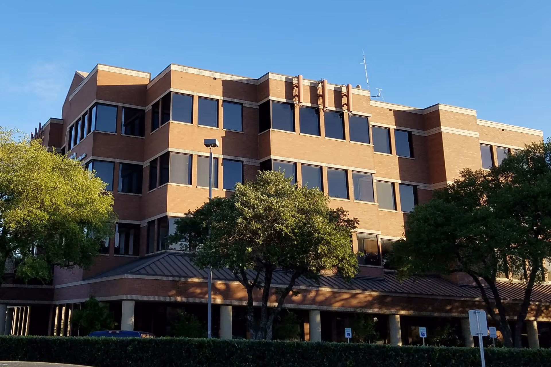 Three-story brick building with large windows and surrounding trees under a clear blue sky.