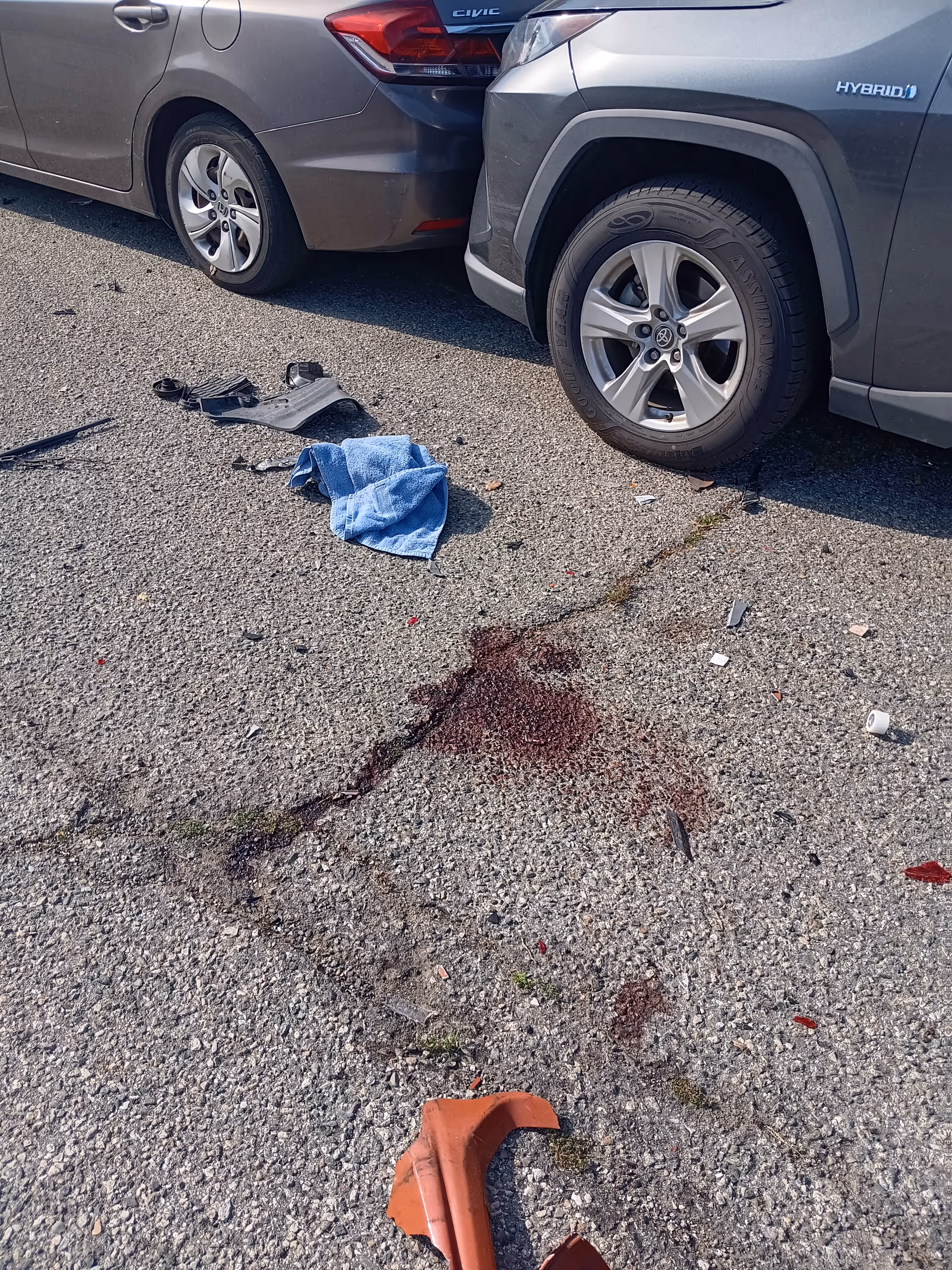 Two parked cars collide in a parking lot with debris and a blue cloth on asphalt.