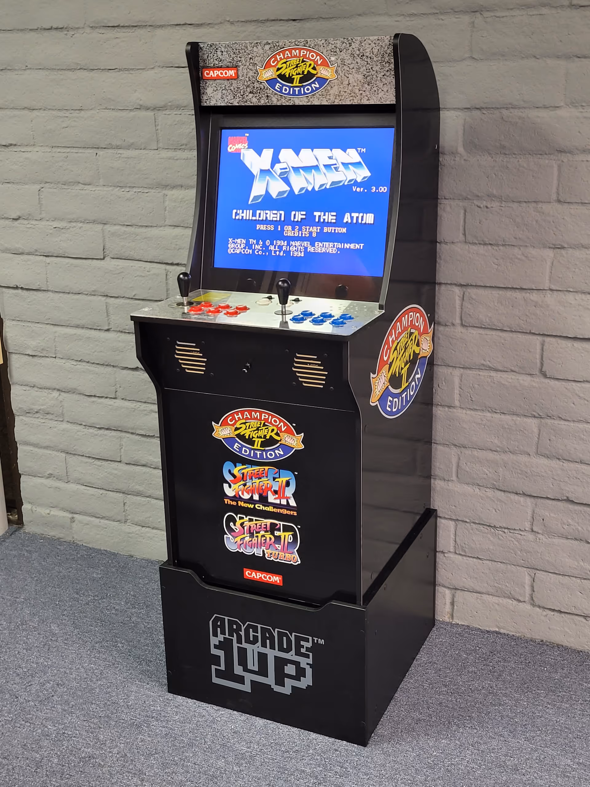 An arcade game cabinet stands indoors against a gray brick wall.