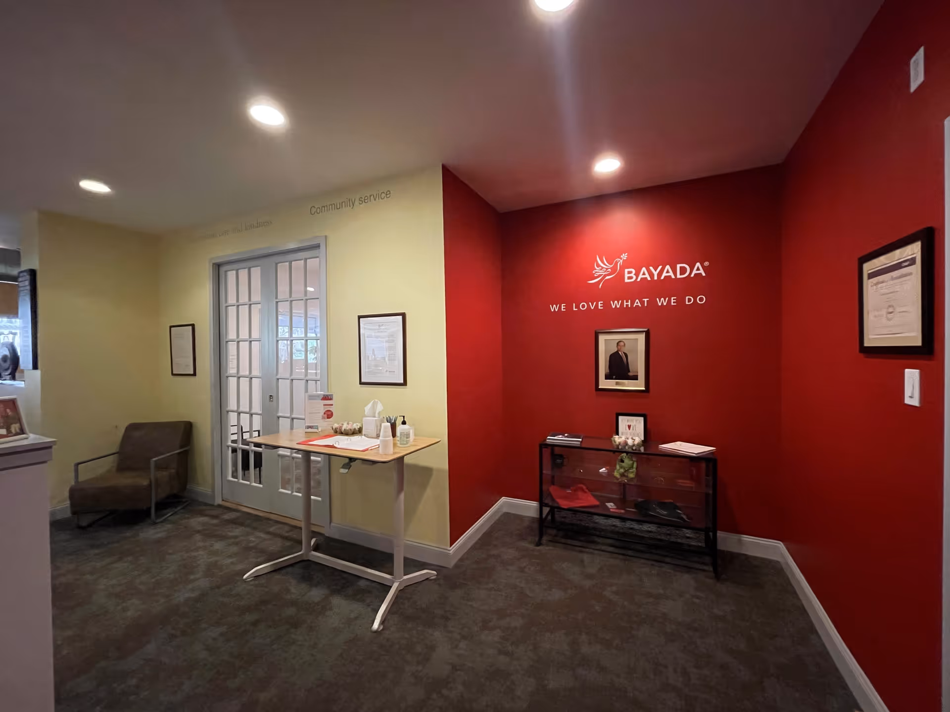 Interior lobby with BAYADA red wall, logo, glass-door entry, table, and seating.
