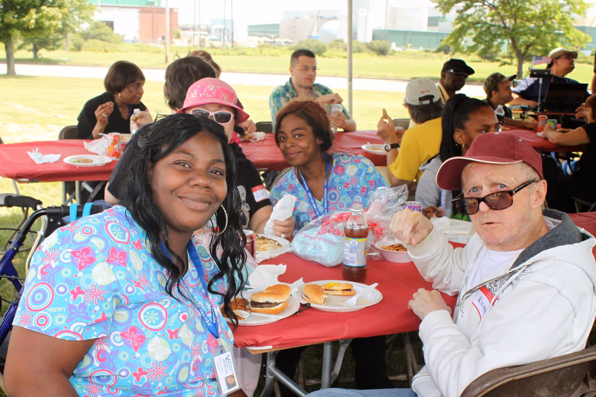 Group of residents and staff share a meal at outdoor picnic tables.