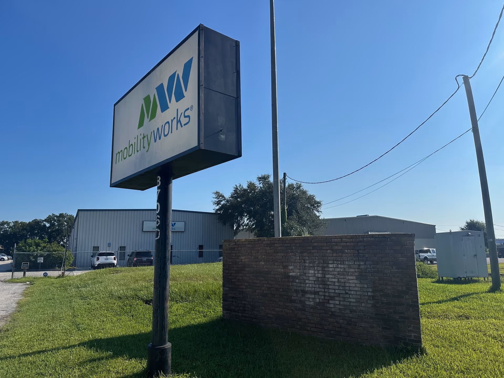 MobilityWorks exterior sign with brick wall and industrial building on a grassy lot.