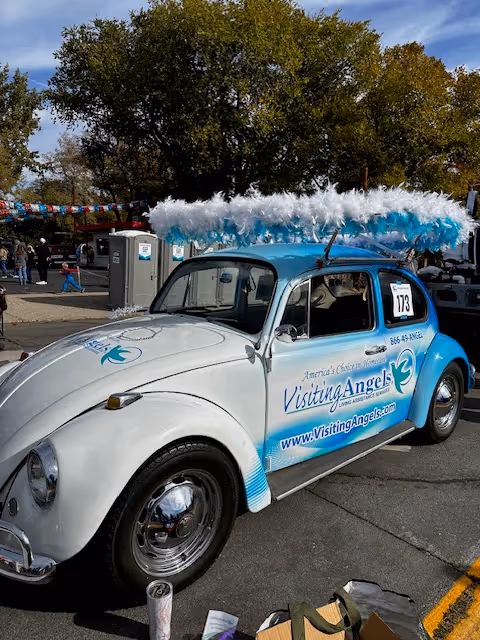 Decorated blue-and-white vintage car with feather boas at a Visiting Angels parade.