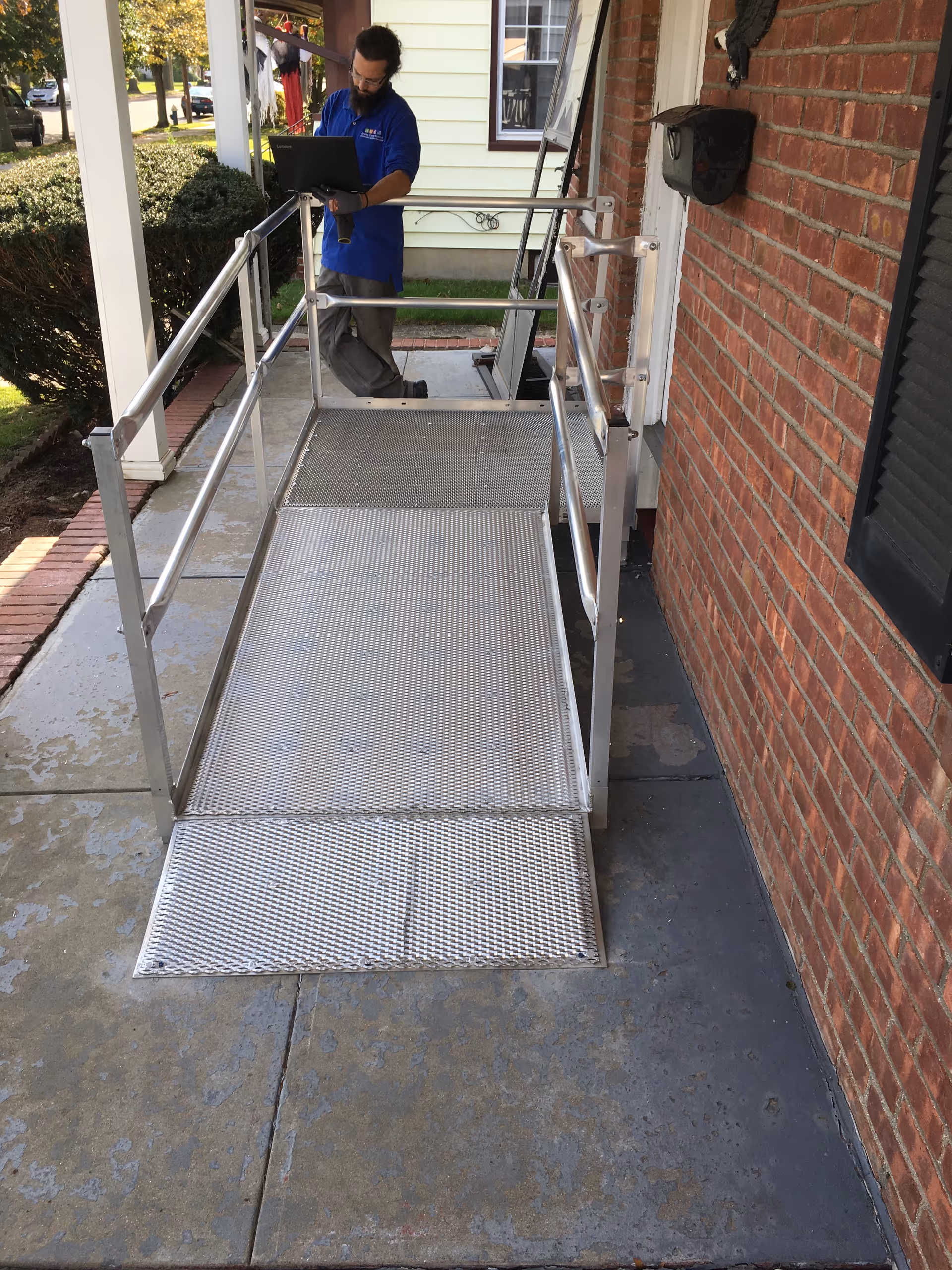 A metal outdoor wheelchair ramp beside a brick building, with a worker using a tablet.