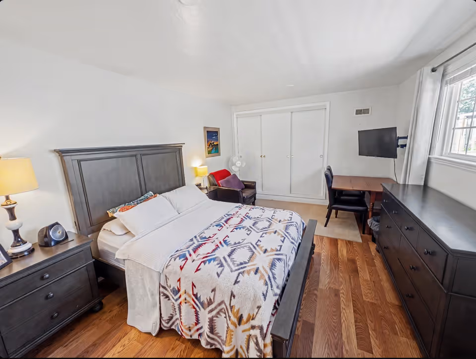 Bright bedroom with a large bed, dresser, desk, and double closet.