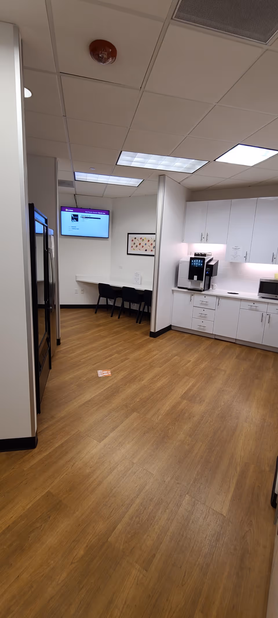 Modern staff kitchenette and break area with white cabinets, coffee machine, and seating.