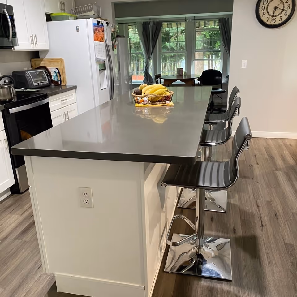 Bright kitchen with a central island, stools, fruit basket, and stainless appliances.