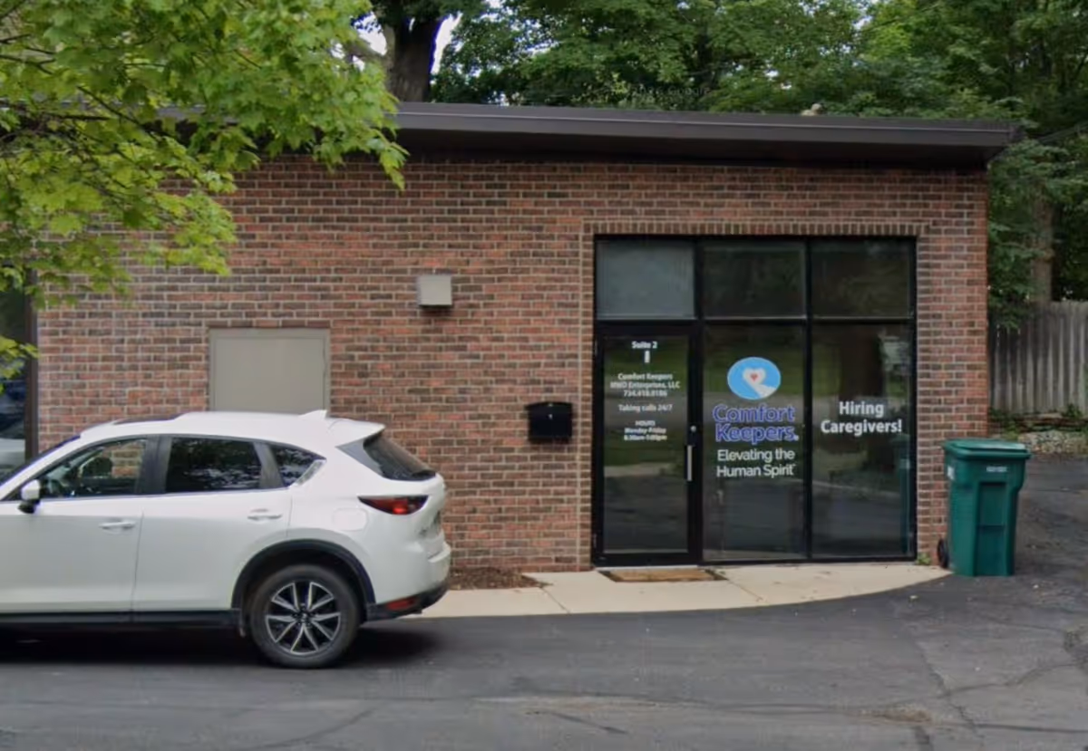 Brick building entrance with glass doors and a white SUV parked in front.