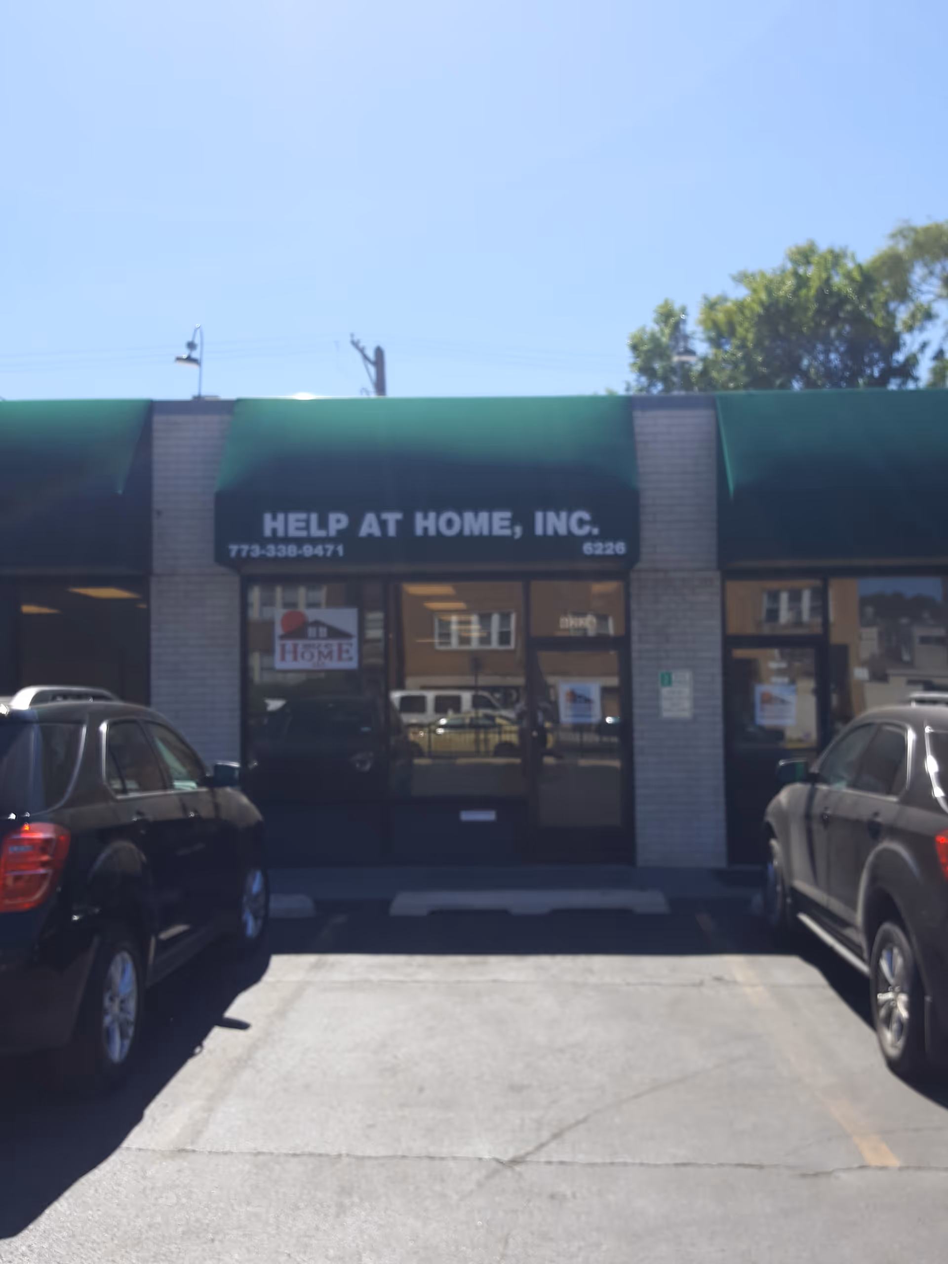 Exterior view of Help at Home storefront with green awnings and parked cars.