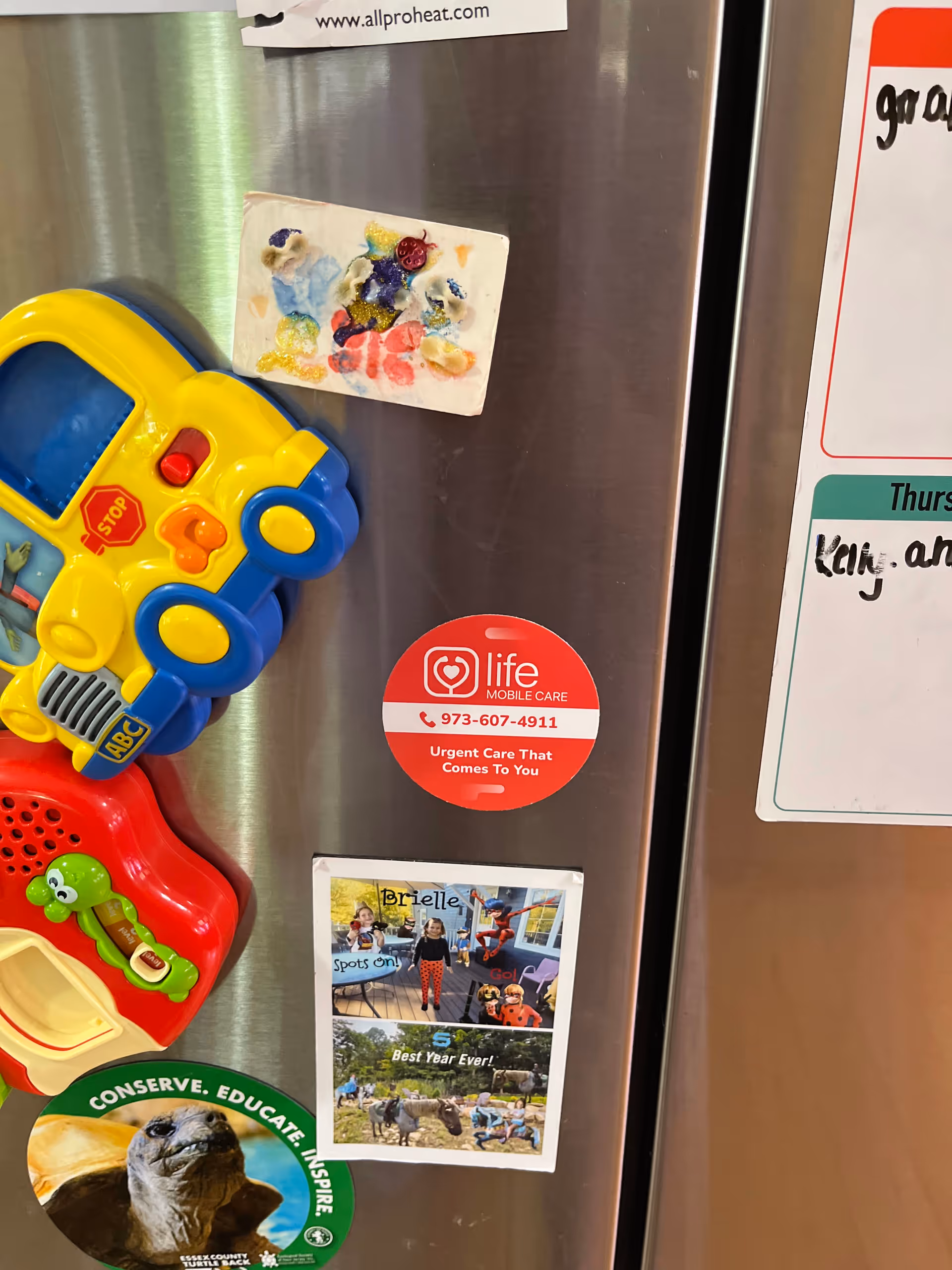 Colorful plastic toys and a Life Mobile Care sticker attached to a metal refrigerator.