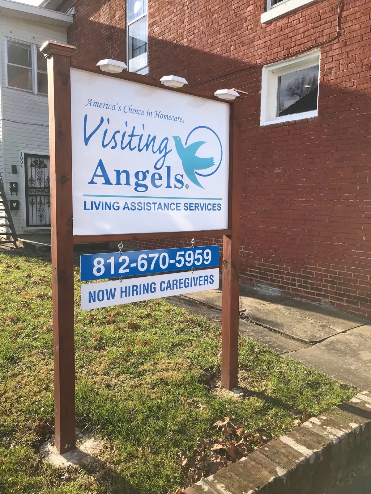 Exterior brick building with Visiting Angels sign and Now Hiring Caregivers banner.