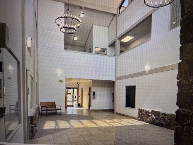 Bright two-story interior lobby with chandeliers, seating bench, tiled floor, and stone accents.