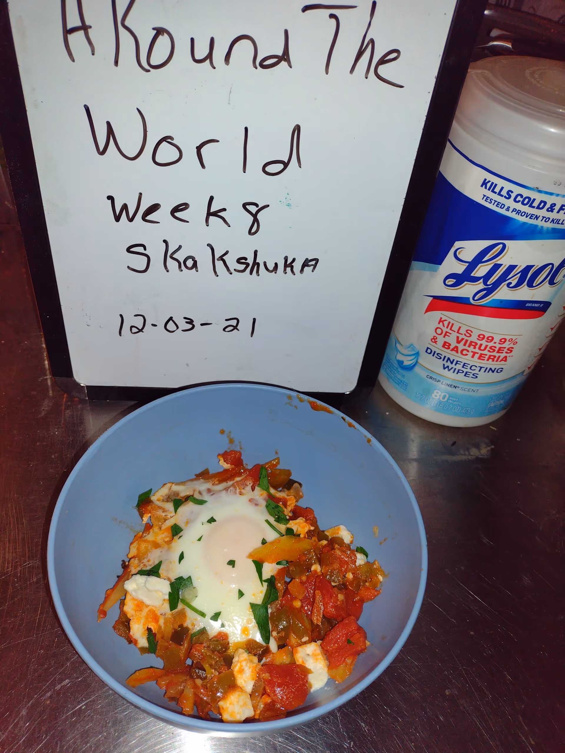 Blue bowl of mixed vegetables and cheese on a stainless counter beside a Lysol bottle.