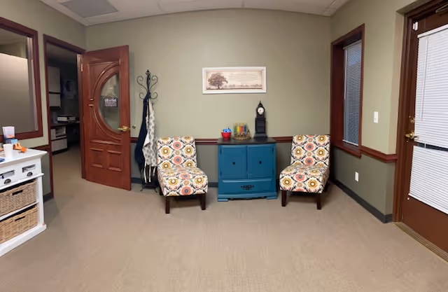 Two patterned armchairs sit opposite a blue cabinet in a small waiting area.