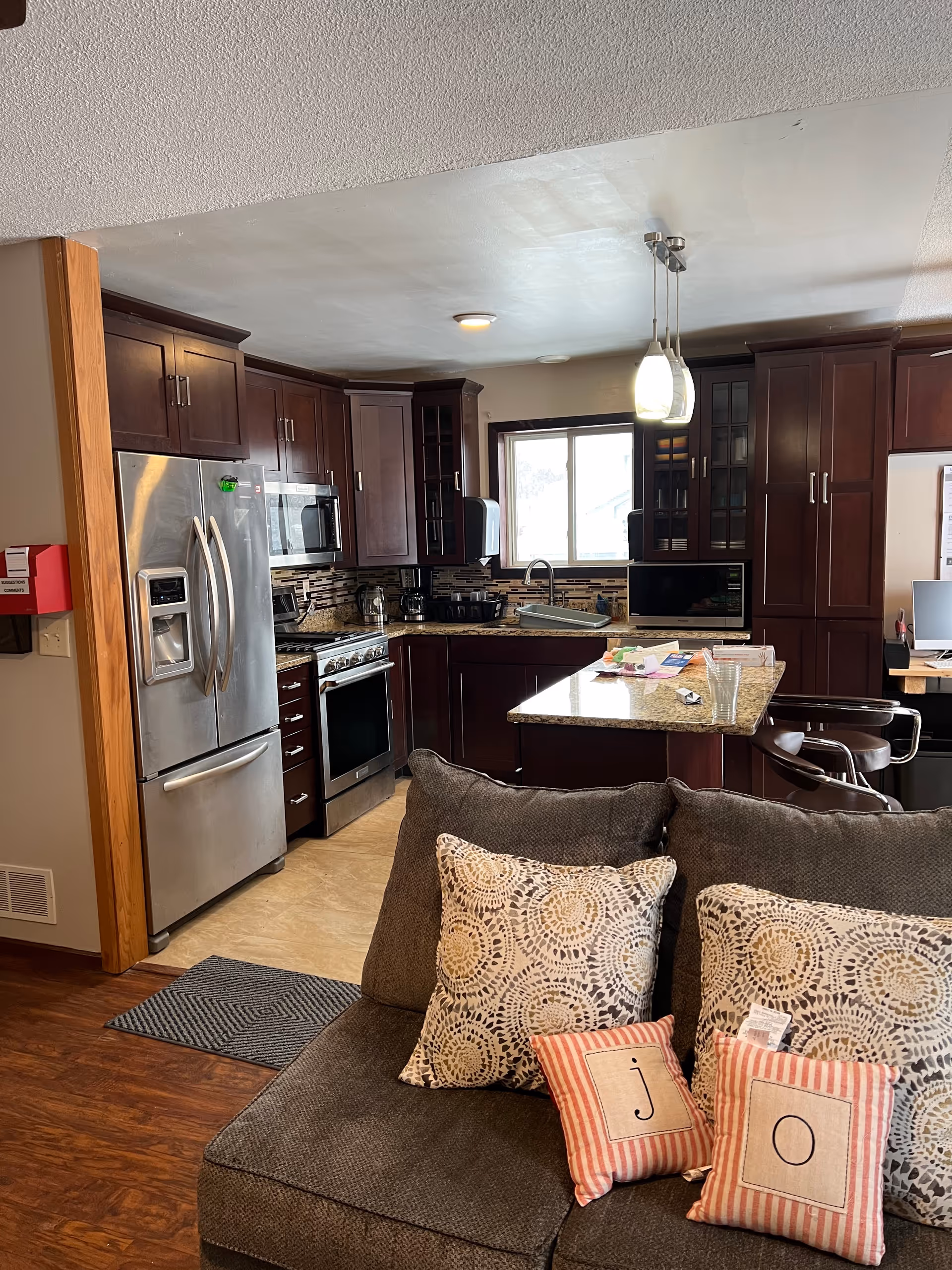 Open-concept kitchen with dark wooden cabinets, stainless appliances, granite island, and a sofa in the foreground.