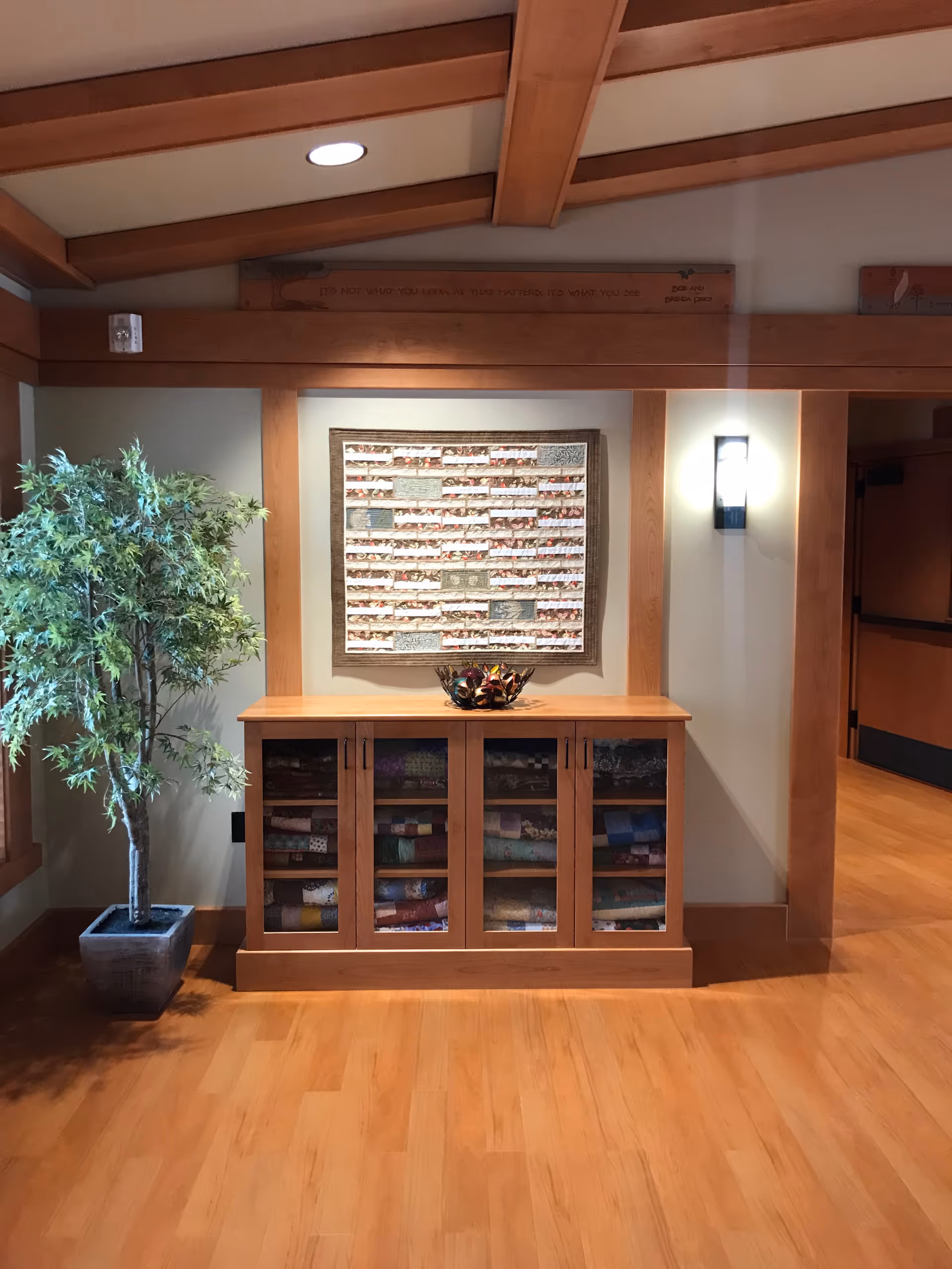 Wooden hallway with fabric cabinet, wall quilt, ceiling beams, and potted plant.