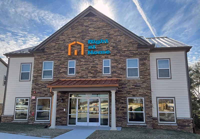 Front view of a two-story stone-faced senior living facility with Right at Home sign.