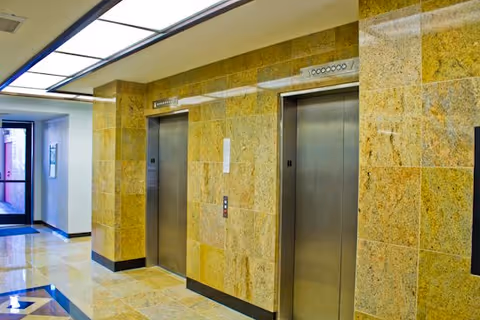 Interior hallway with two elevator doors along a tiled stone wall in a lobby