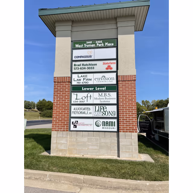 Tall outdoor signboard with multiple business names outside a Compassus facility under blue sky.