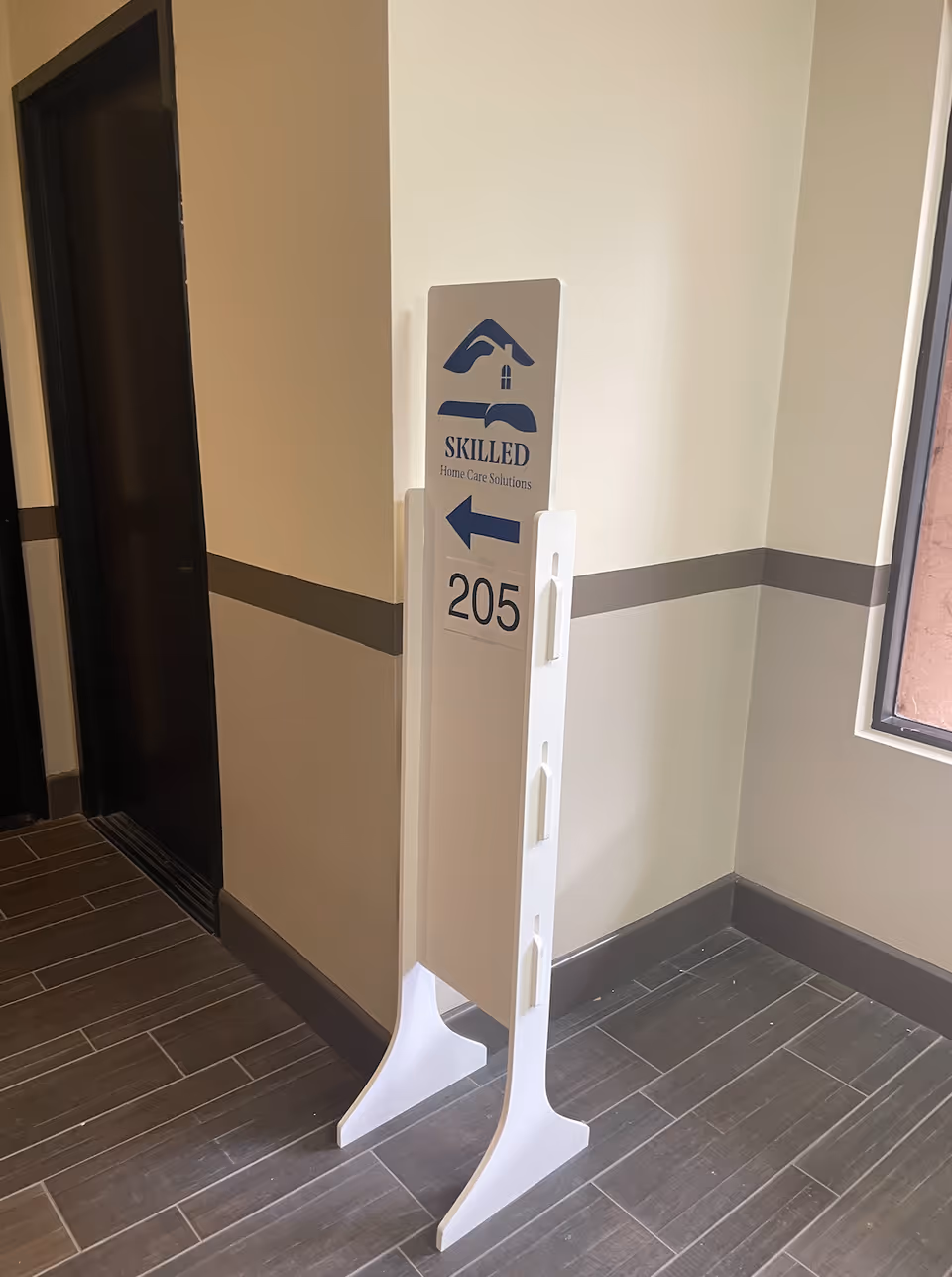 Interior hallway with a tall white sign directing to room 205 at Skilled Home Care Solutions