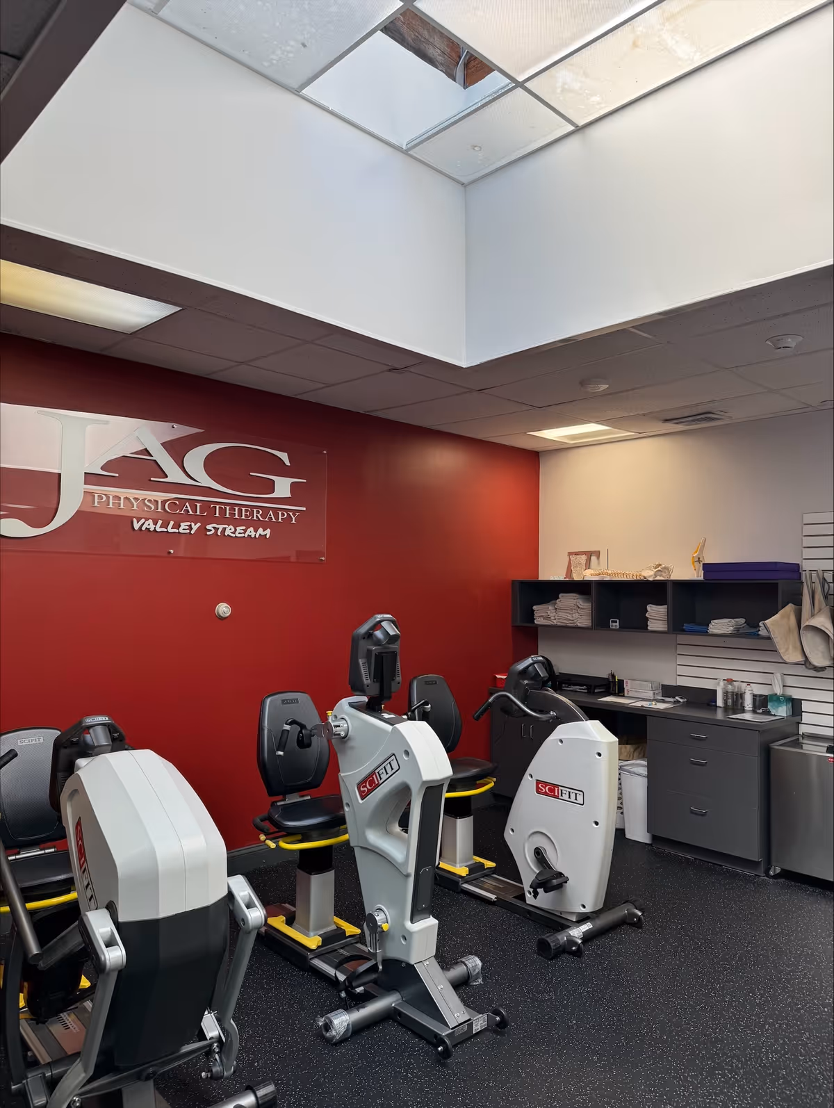 Interior physical therapy room with exercise bikes, a red wall, and a JAG Physical Therapy sign.